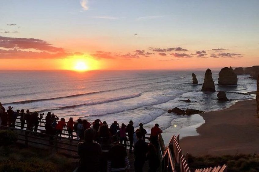 A sunset over the ocean with rock formations and a crowd of people on the beach. 2