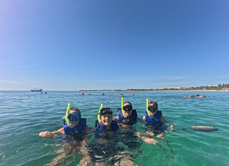 Four people snorkeling in clear blue water with a boat and other swimmers in the background. 3