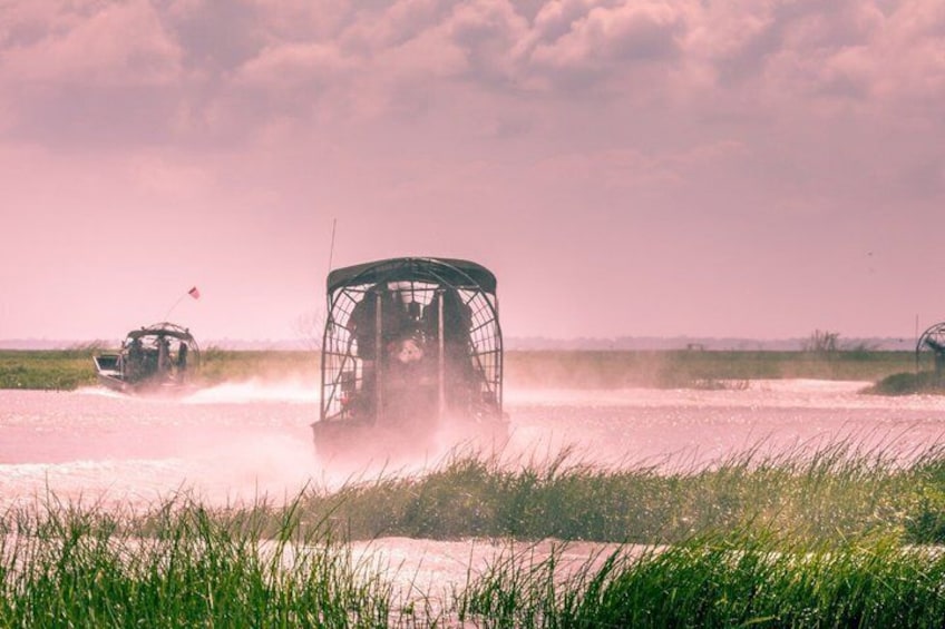 A vehicle driving through a shallow water body, surrounded by grass. 1
