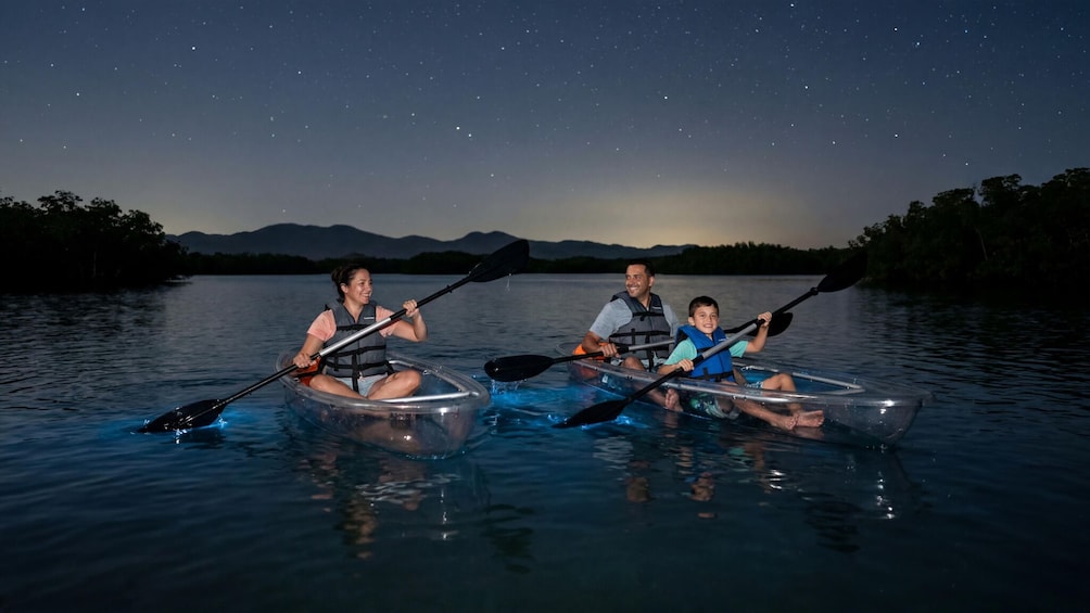 Trois personnes pratiquent le kayak sur un lac paisible, de nuit, et les étoiles sont visibles dans le ciel. 1