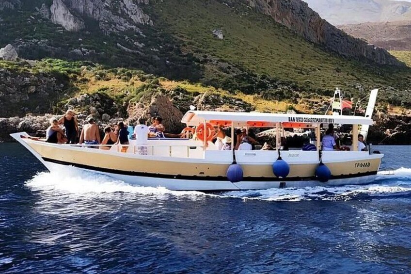 A boat with passengers, moving through a body of water with rocky cliffs in the background. 1