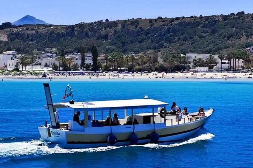 A boat on a clear blue sea with a beach and hills in the background. 5