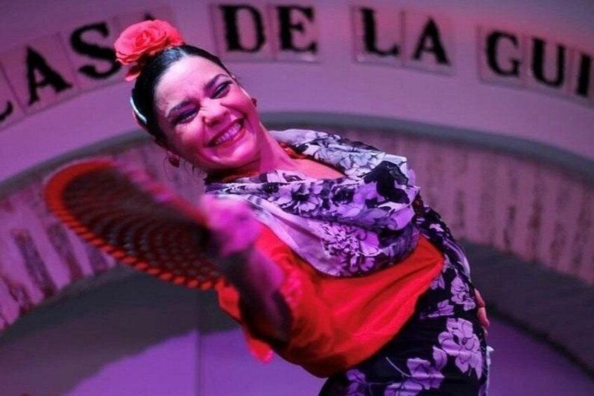 Une personne portant une robe à motifs et un accessoire floral rouge, debout devant un panneau dont le texte est partiellement visible. 2