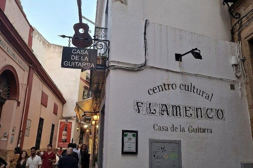 A narrow street with a sign for 'Casa de la Guitarra' and 'centro cultural flamenco' on a building. 2