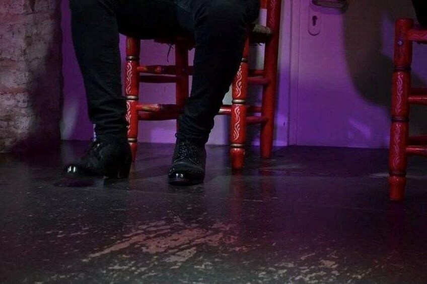 A person sitting on a red chair with a patterned design, wearing black pants and black shoes. 2