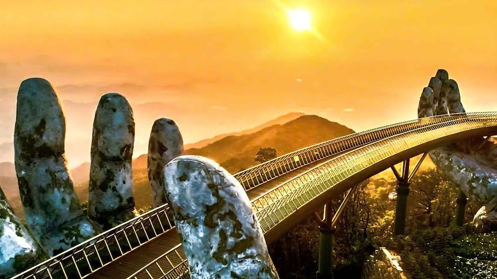 A bridge with a unique design, surrounded by large rock formations and mountains under a sunset sky. 1