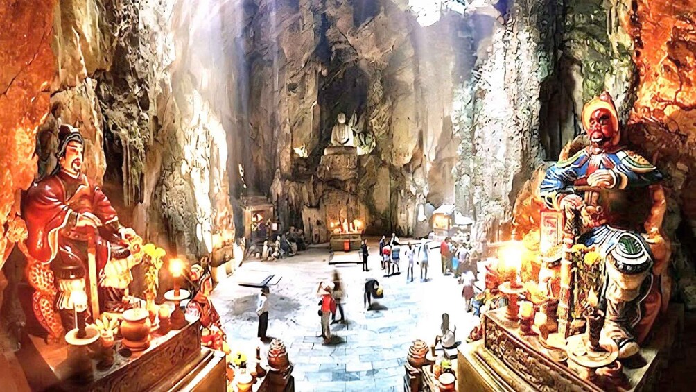 A cave interior with statues, a central altar, and visitors. 3