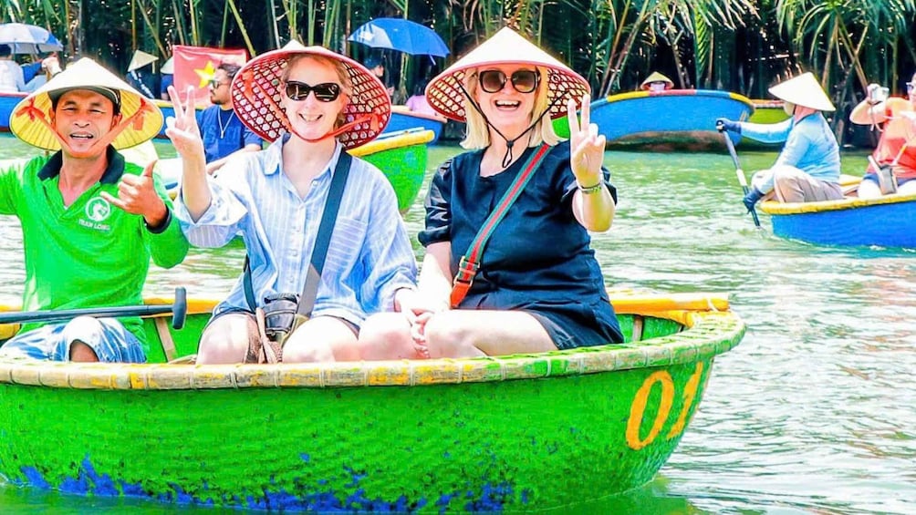People in a green boat with a number '01' on it, wearing conical hats, on a body of water with other boats and greenery in the background. 5