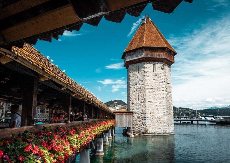 A stone tower by a waterfront with a covered walkway and colorful flowers. 1
