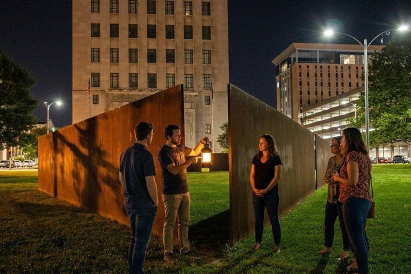 Un grupo de personas de pie en un césped, con edificios al fondo. 1