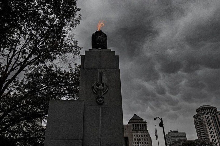 A tall monument with a flame on top, surrounded by trees and buildings. 3