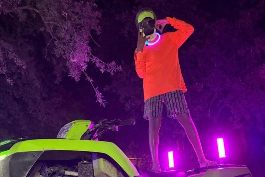 A person in a red shirt and striped shorts standing on a vehicle with neon lights. 3
