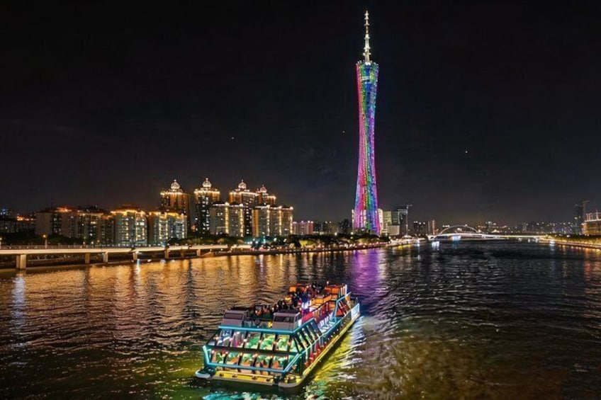 A brightly lit boat on a river with a city skyline and a tall tower in the background. 3