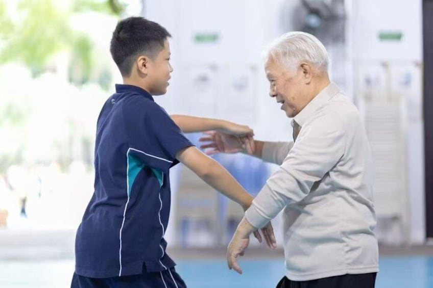 Two people engaging in a physical activity, likely a form of exercise or therapy, in an indoor setting with exercise equipment in the background. 4
