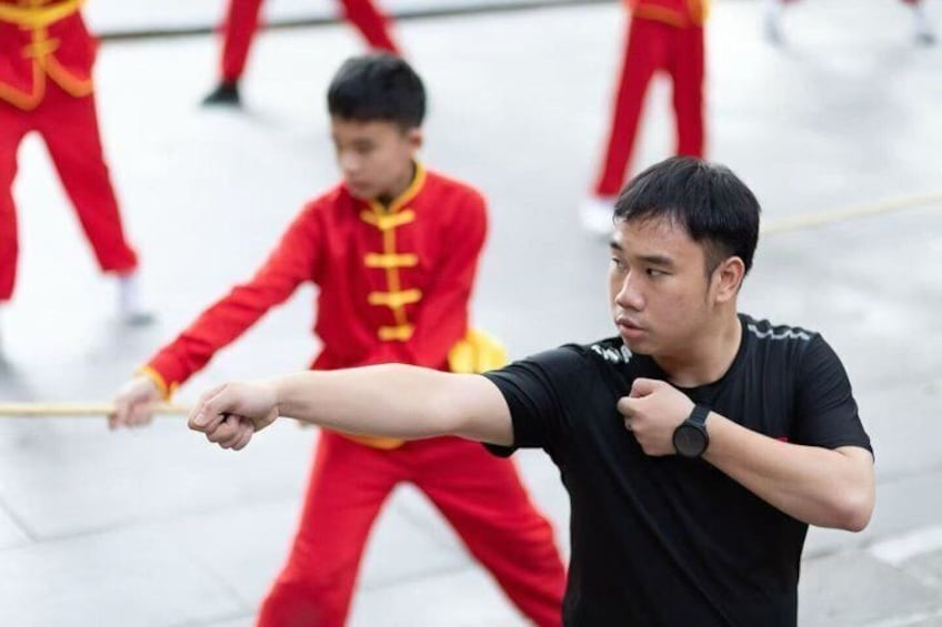 A person in black attire practicing Tai Chi with a child in red attire in an outdoor setting. 5