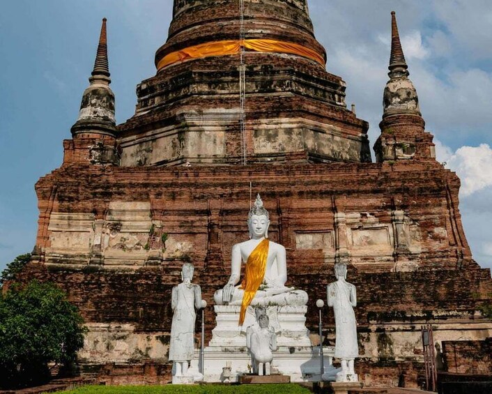 A large Buddha statue in front of a temple with a golden aura and three smaller statues. 1