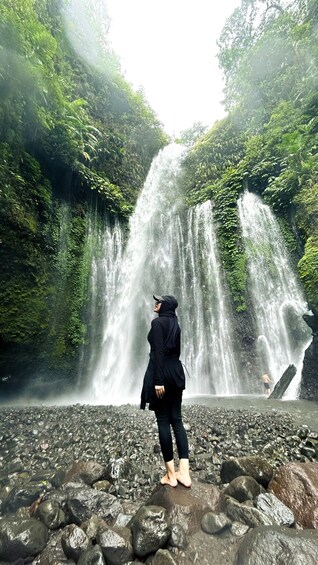 A person standing on rocks facing a waterfall. 1