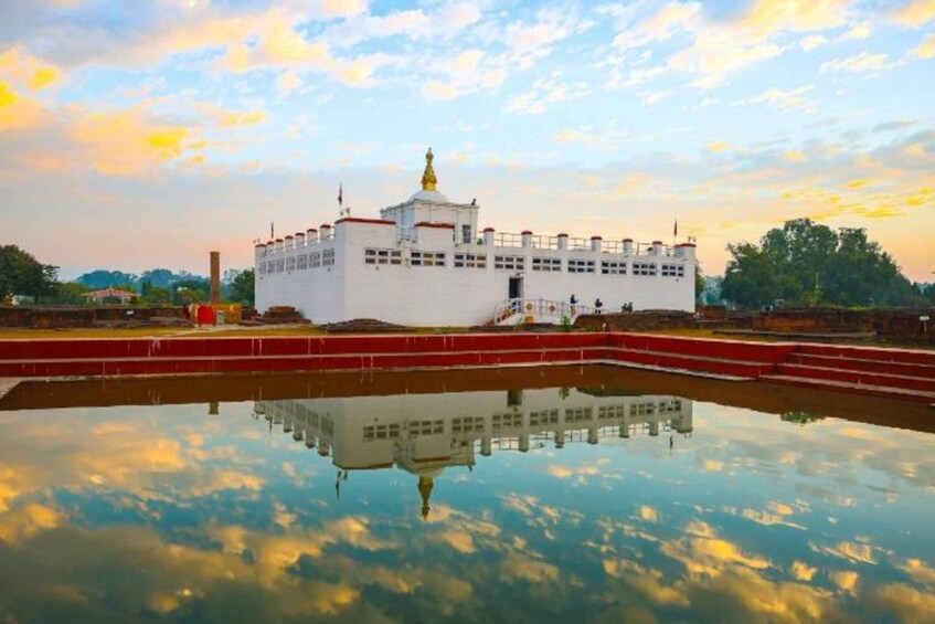 A white building with a golden spire, reflecting in a calm body of water, surrounded by greenery. 1