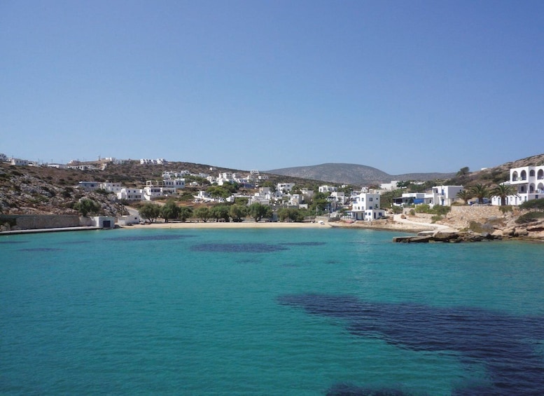 A coastal town with white buildings, clear turquoise waters, and a hilly backdrop. 1