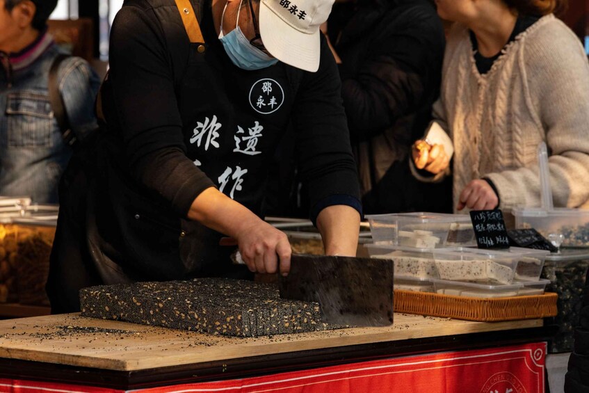 A person slicing a black, textured food item on a wooden cutting board. 2
