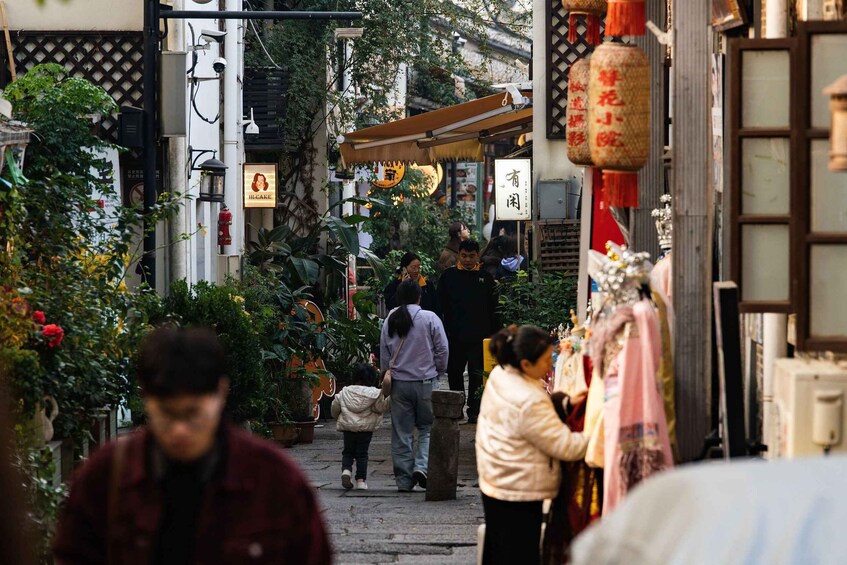 A narrow street with people walking, shops on either side, and traditional decorations. 1