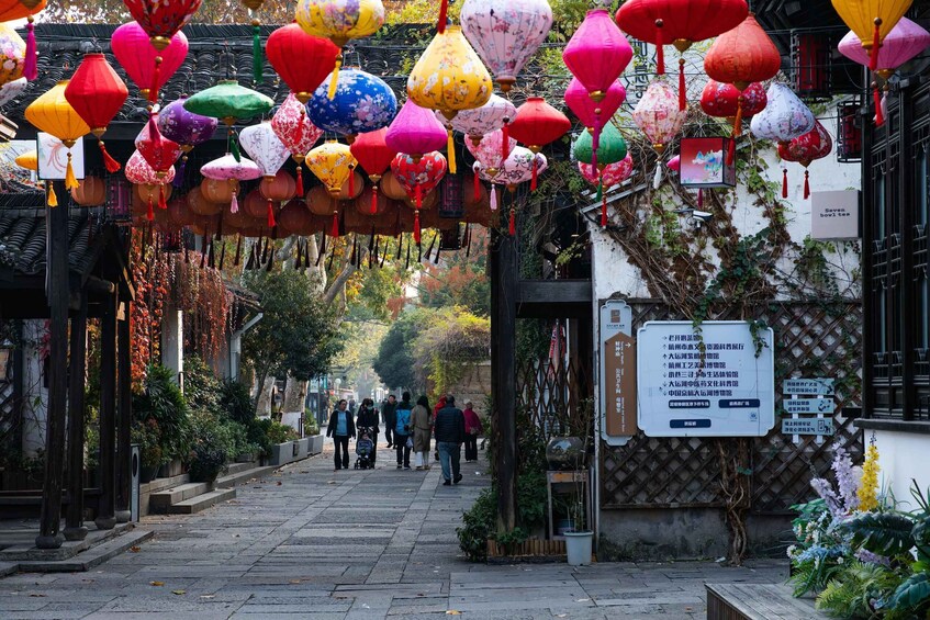 A street with colorful lanterns hanging overhead, people walking, and a signboard on the right. 3