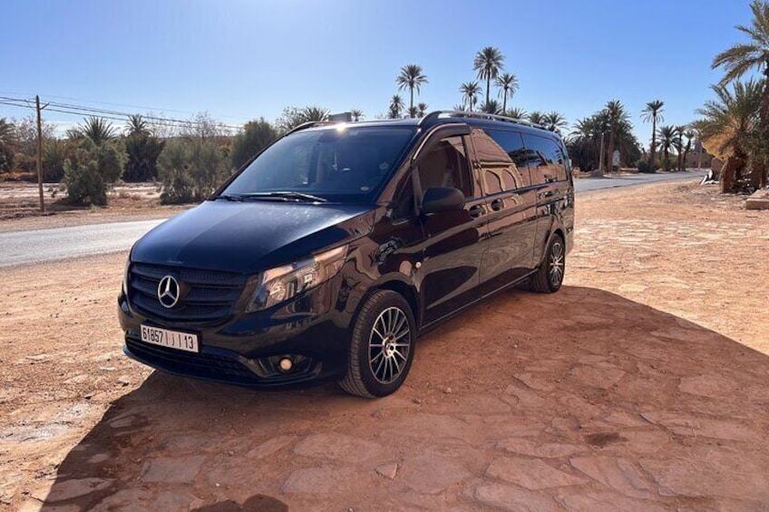 A black Mercedes-Benz van parked on a dirt road with palm trees and a clear sky in the background. 3