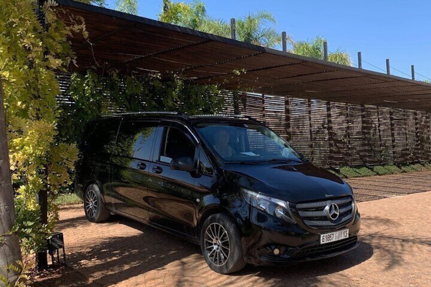 A black Mercedes-Benz SUV parked under a covered area with a wooden fence and greenery in the background. 2