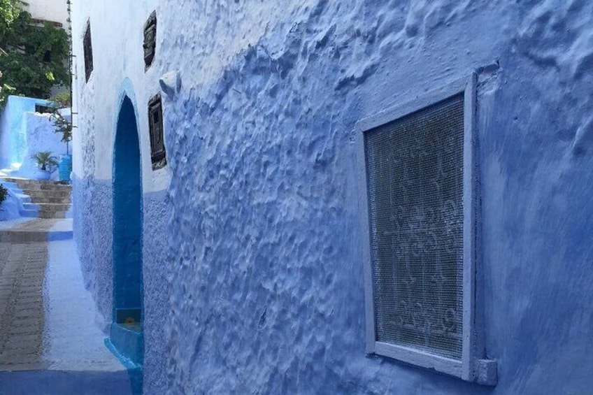 A building with a textured blue exterior, a window with a metal screen, and a blue archway. 5
