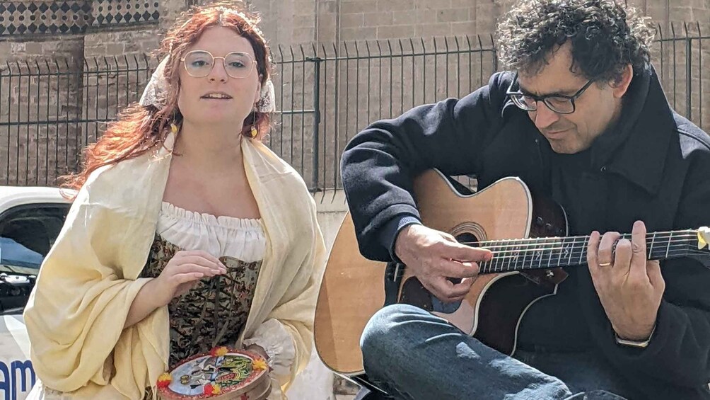 A person playing an acoustic guitar and another holding a plate with food. 1