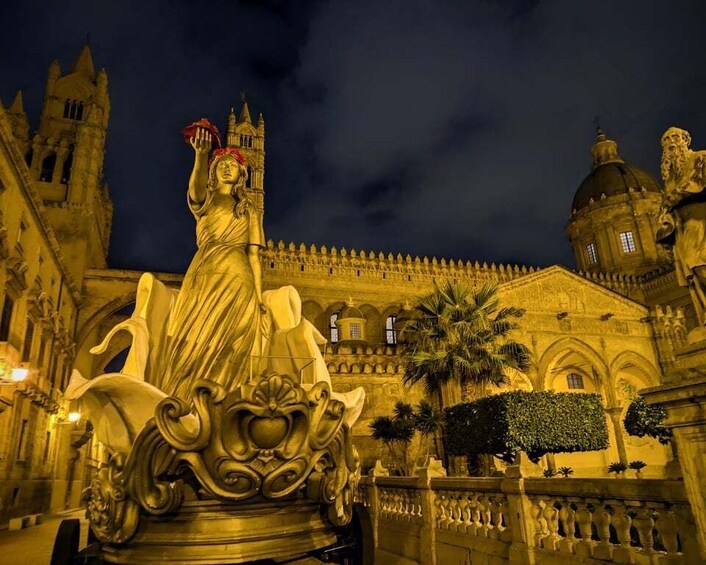 A statue of a woman holding a heart, set against a historic building with arches and a tower. 2