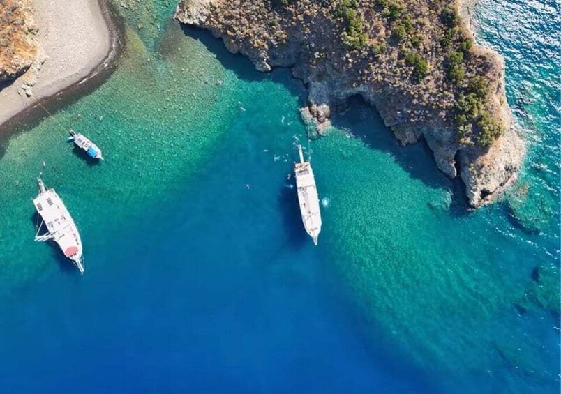 Three boats anchored near a rocky coastline with clear blue waters. 3
