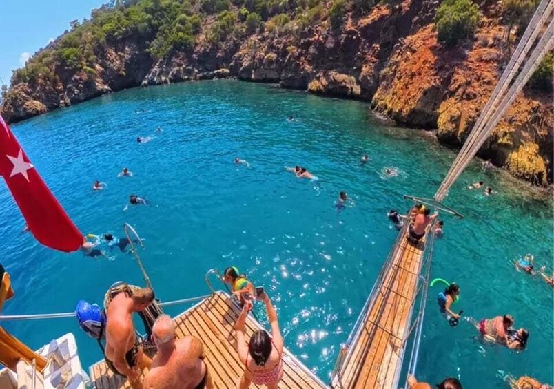 A group of people swimming in a clear blue sea with rocky cliffs in the background. 5
