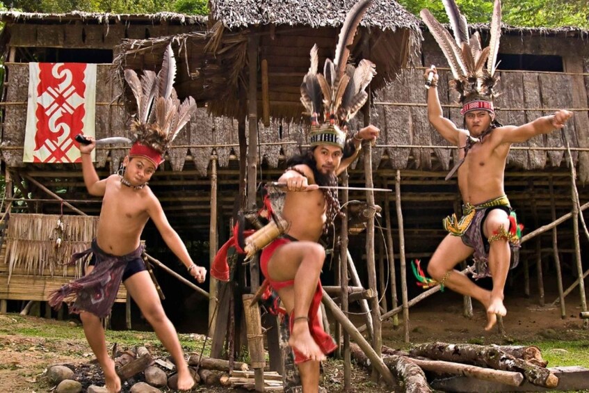 Three individuals in traditional attire performing an acrobatic stunt in front of a rustic structure. 1