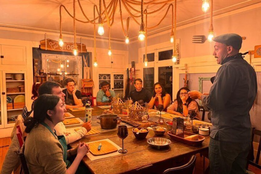 A group of people dining in a warmly lit kitchen with hanging lights and a rustic wooden table. 2