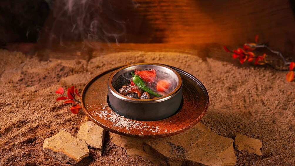 A traditional clay pot with food, surrounded by a rustic setting with sand and scattered leaves. 5