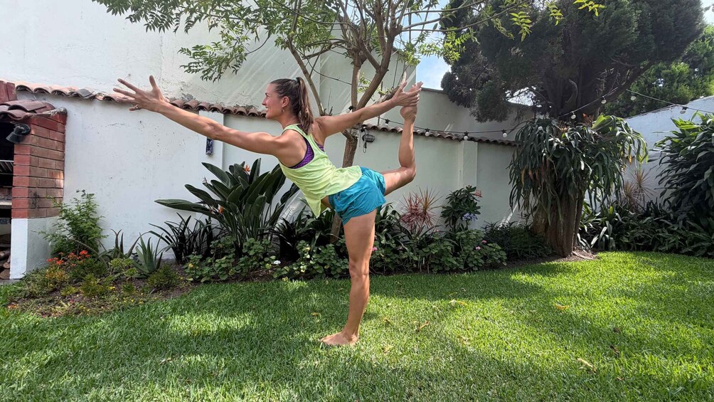A person performing a yoga pose outdoors on grass with a garden and trees in the background. 5