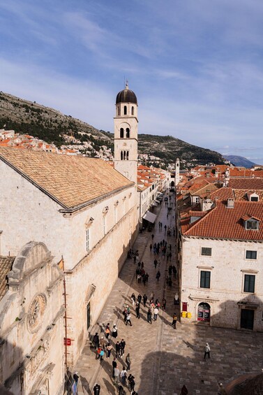 A historic square with a prominent tower, stone buildings, and a hilly backdrop. 3