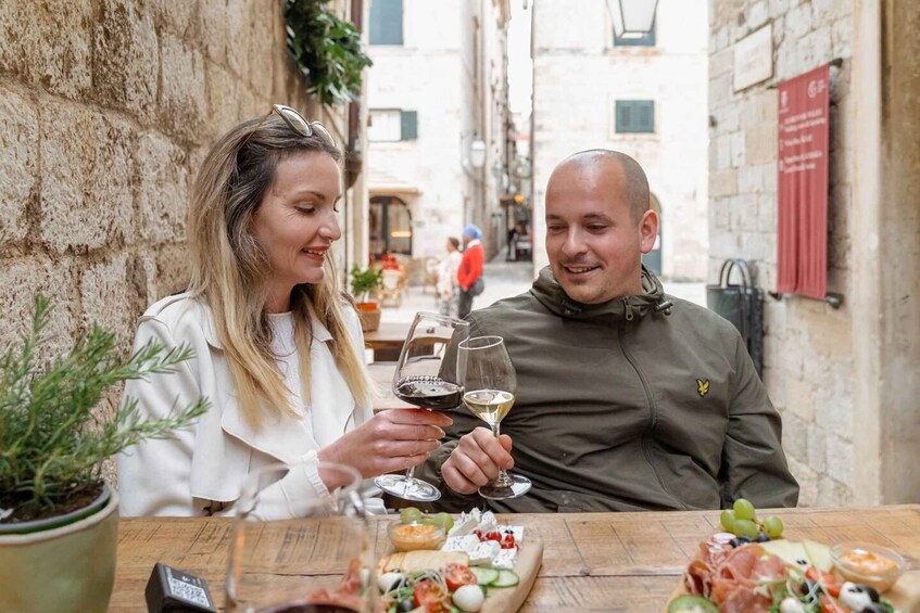 Two people toasting with wine glasses at a table with a variety of cheeses and meats. 2