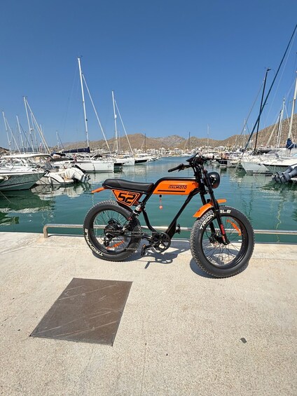 A stationary electric bike with 'ITALMOTO' branding parked by a marina with boats and hills in the background. 2