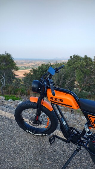 A parked motorcycle with a visible brand name, a front view of the handlebars, and a scenic landscape in the background. 4