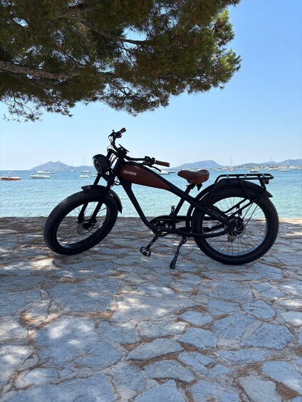 A stationary electric bike parked on a stone pavement by the sea, with boats and a clear sky in the background. 5