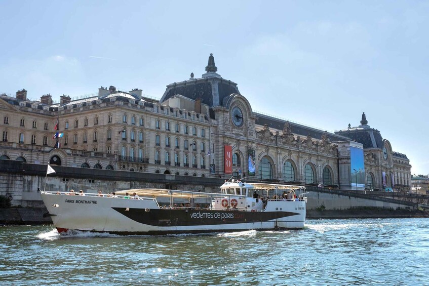 En båt med namnet ”Paris Montmartre” ligger i floden, och i bakgrunden syns en stor, historisk byggnad. 3