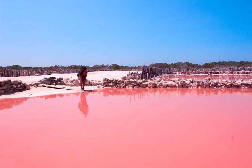 A person standing by a red-pink water body with a wooden fence in the background. 1
