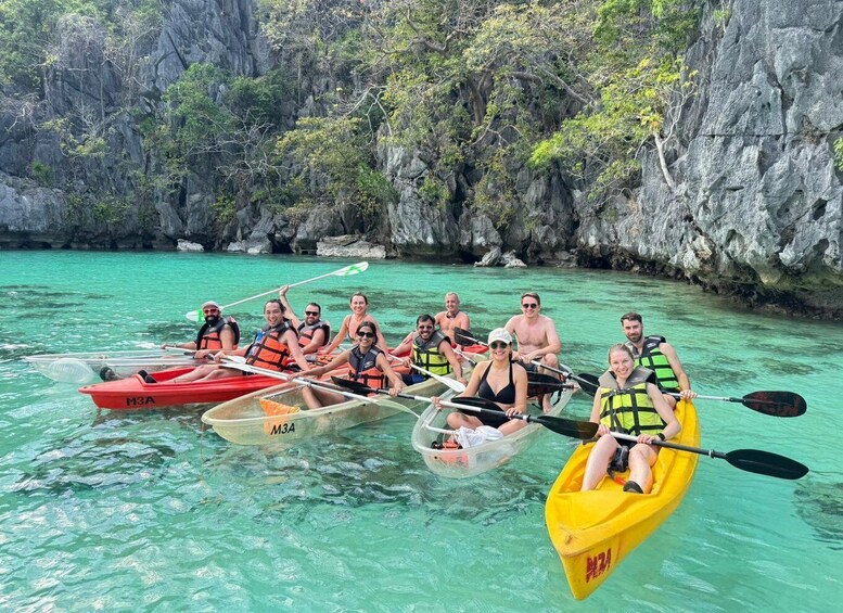 A group of people kayaking in clear turquoise waters with rocky cliffs in the background. 1