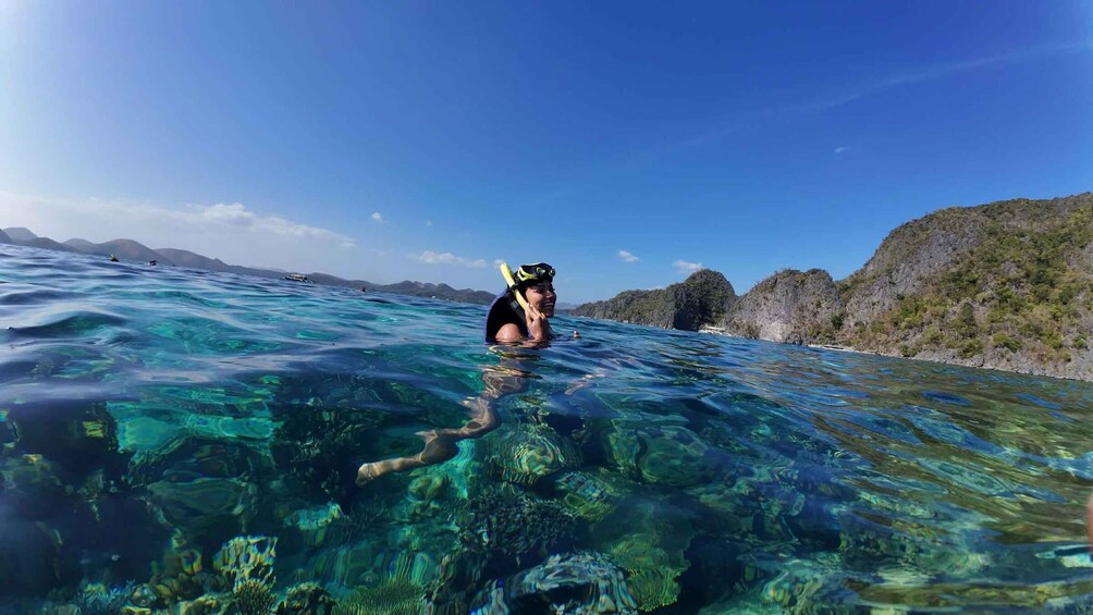 A person snorkeling in clear blue water with rocky hills in the background. 1