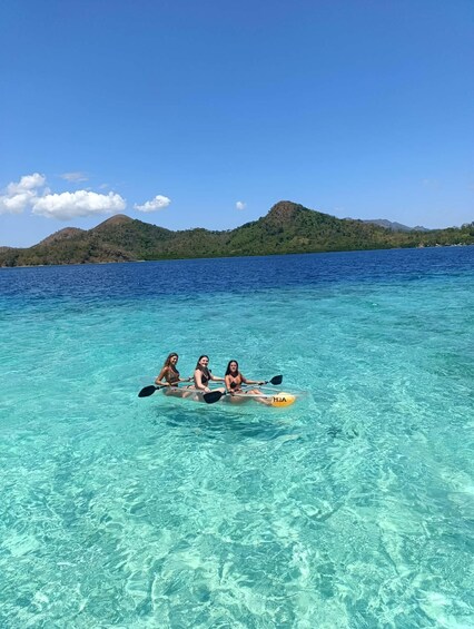 Three people kayaking on a clear blue sea with mountains in the background. 4