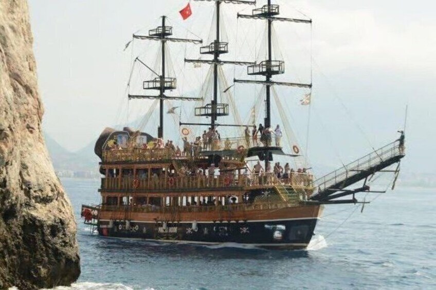 A historical ship with multiple decks and passengers, sailing near a rocky coastline. 4