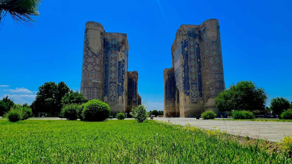 Two tall, intricately patterned towers in a lush green field under a clear blue sky. 2