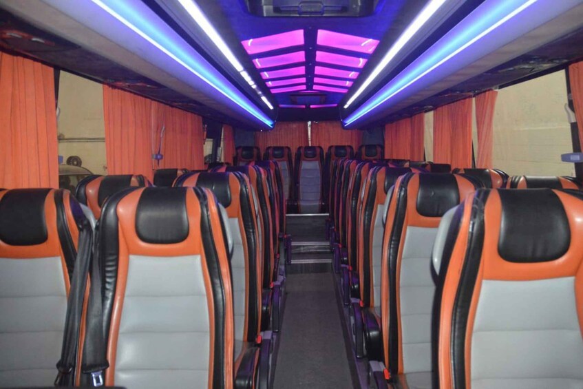 A train interior with orange and black seats, purple lighting, and curtains on the windows. 2